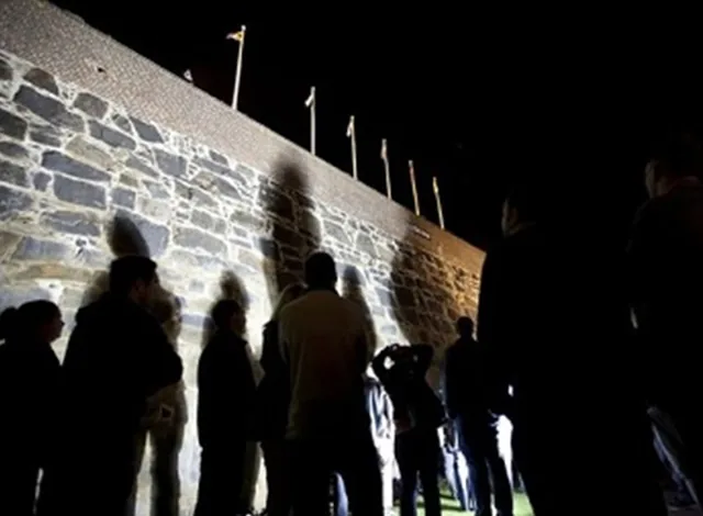 Guests cast long shadows on historic stone walls during a night tour