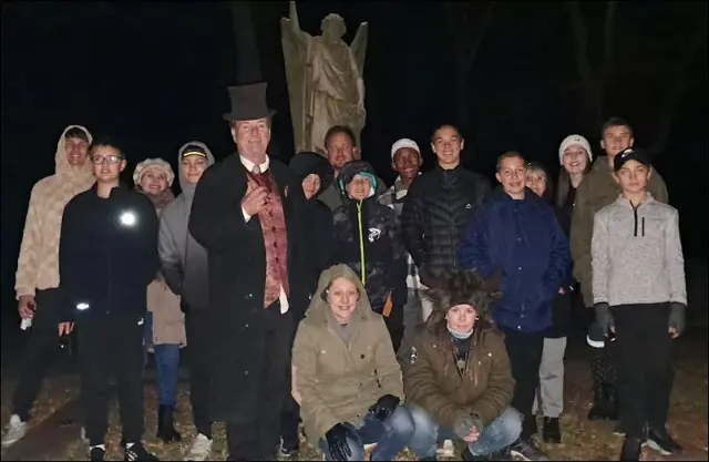 A smaller group posing with a top-hatted host at night