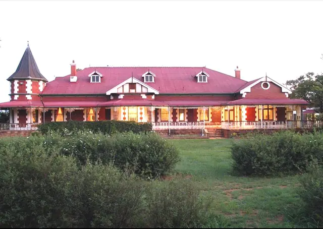 Long historic house with a red roof and illuminated veranda