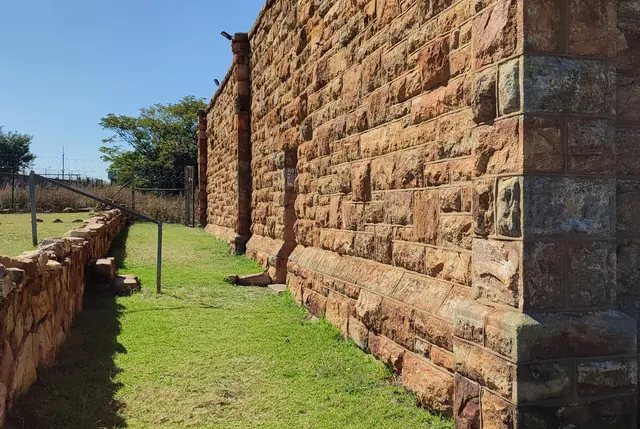 Sandstone jail wall beside a grassy passage